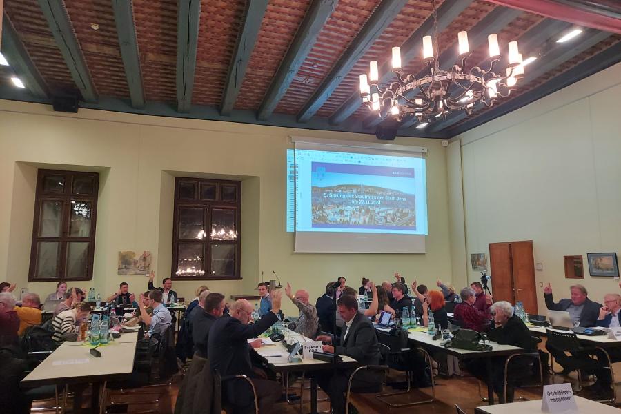 Stadtratsmitglieder im Historischen Rathaus sitzen an Tischen und verfolgen die Debatten