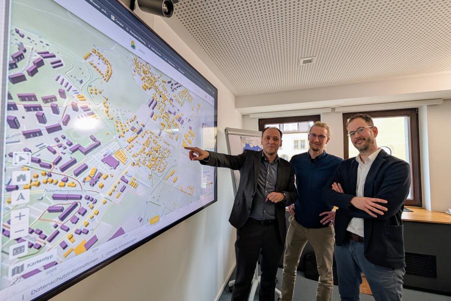 Christian Gerlitz, Bürgermeister und Dezernent für Stadtentwicklung und Umwelt der Stadt Jena, Kevin Muschalle-Momberg Klimaschutzkoordinator der Stadt Jena, und Christian Dornack, Bereichsleiter Strategie bei den Stadtwerken Jena Netze stehen vor einer Karte der Kommunalen Wärmeplanung.