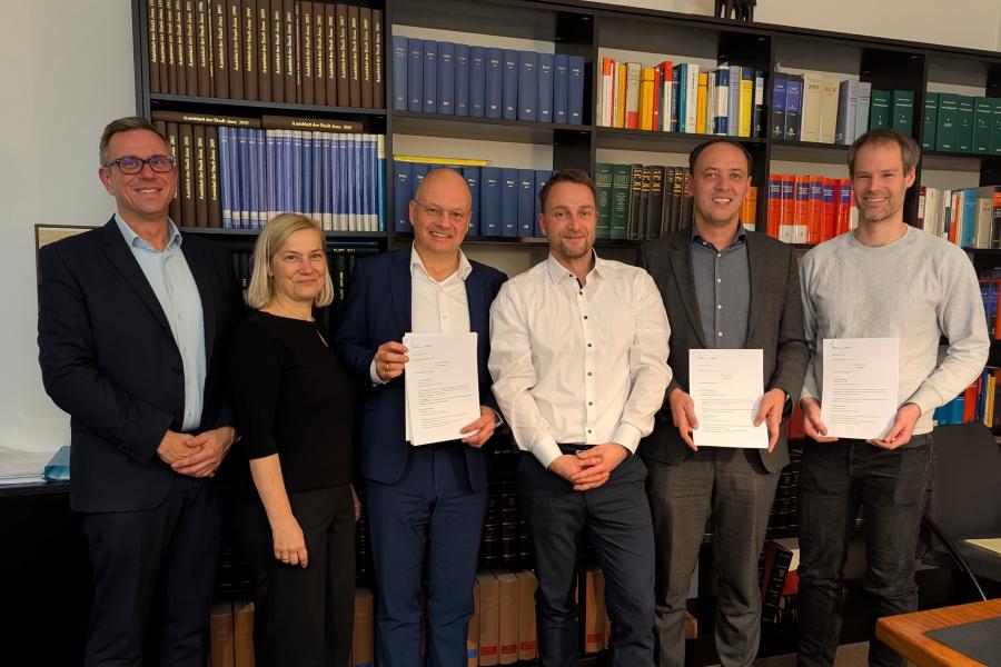 v.l.: André Sack, Claudia Budich, Tobias Wolfrum, Hermann Zebisch, Christian Gerlitz und Dr. Simon Münch stehen vor einem Bücherregal mit den unterzeichneten Vertrag