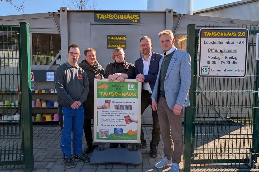 Vor dem Tauschhaus 2.0 stehen 5 Personen um ein Aufsteller, der Hinweise zu Gegenständen im Tauschhaus gibt.