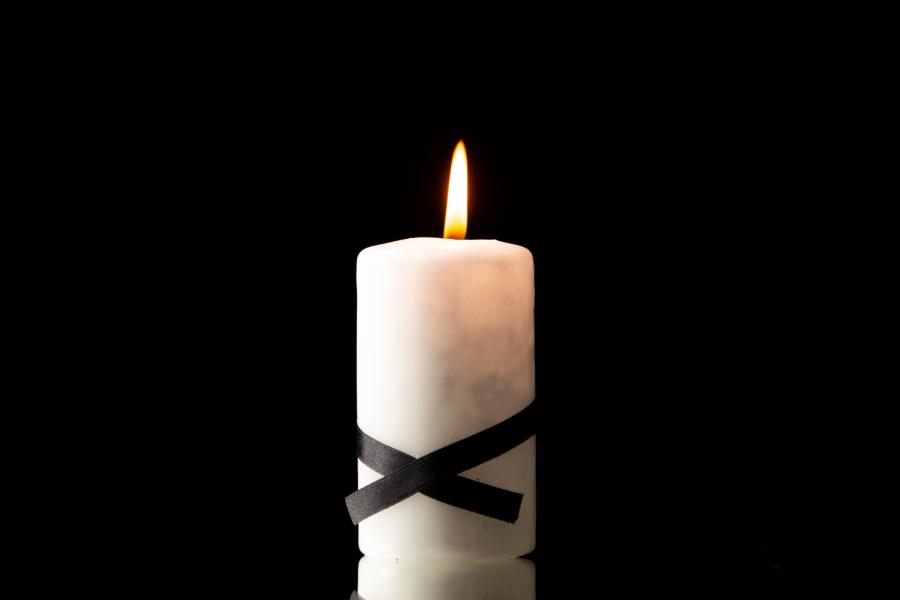 Eine weiße Kerze mit schwarzen Kreuz steht vor einem schwarzen Hintergrund und brennt.