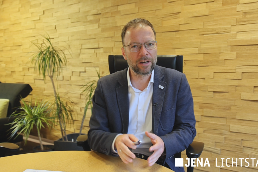 Oberbürgermeister Thomas Nitzsche sitzt in seinem Dienstzimmer am Beratungstisch und spricht in die Kamera.