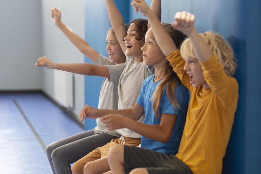 Kinder jubeln am Spielfeldrand in einer Sporthalle.