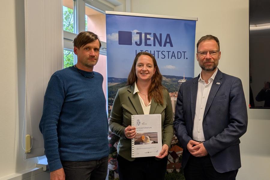 Zwei Männer und eine Frau stehen nebeneinander vor einem Roll-Up der Stadt Jena.