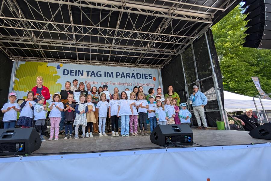 Auf einer Bühne stehen eine Reihe von Kindern und Jugendliche plus einige Erwachsene.