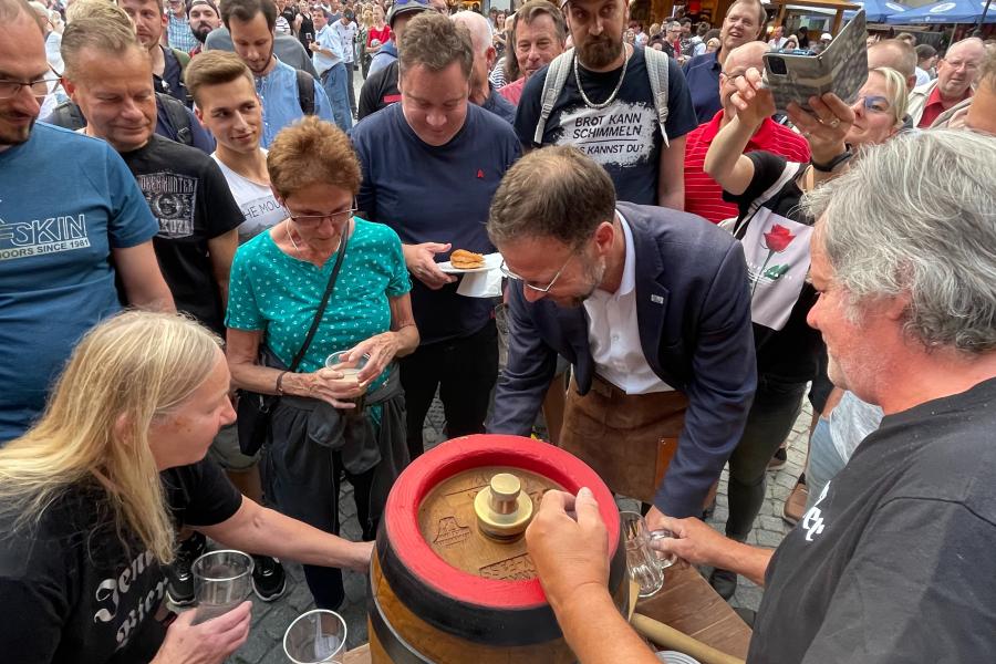 Ein Mann sticht ein Bierfass an, viele Menschen beobachten ihn