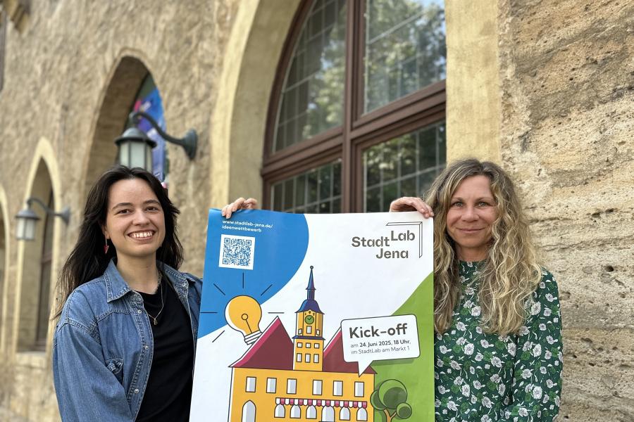 2 Frauen halten vor StadtLab Veranstaltungsplakat hoch