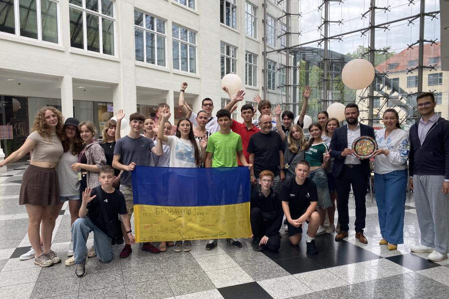 Einen Gruppe von Jugendlichen steht mit ein paar erwachsenen für ein Gruppenfoto zusammen und halten eine Ukraine-Flagge.