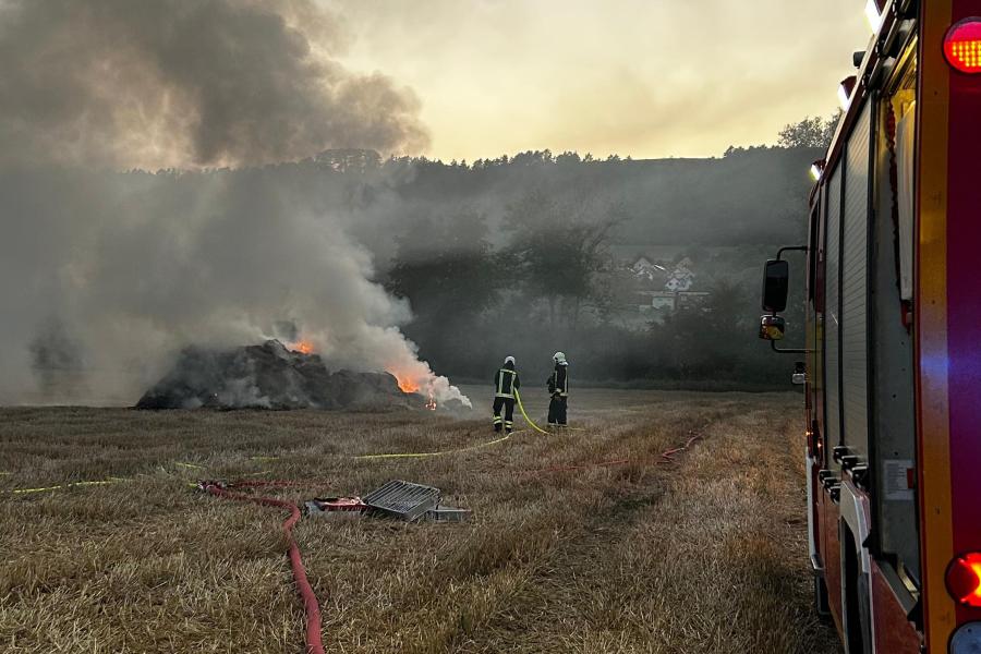 Feuerwehrauto auf einem Feld mit starkem Rauch und brennenden Strohballen