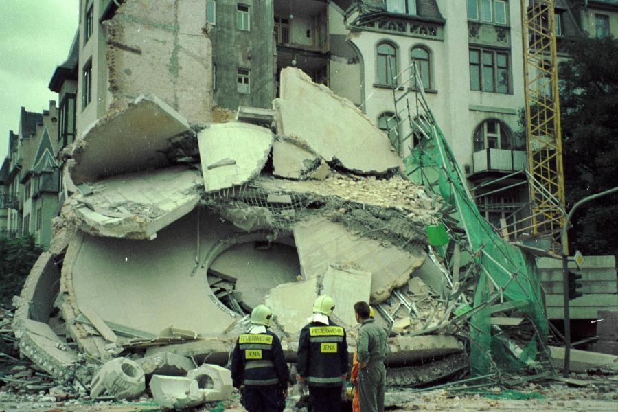 Drei Menschen schauen auf ein eingestürztes Gebäude.