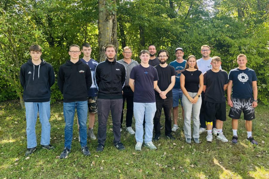 14 Personen stehen für ein Gruppenbild in zwei Reihen neben- bzs. hintereinander