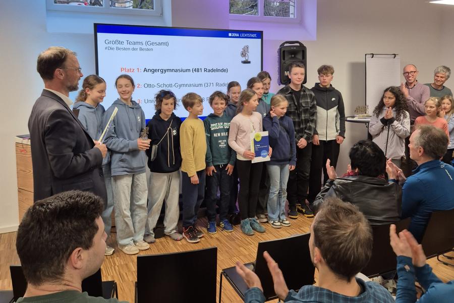 Der Oberbürgermeister steht mit einer Gruppe vor Schülern vor Publikum. Eine Schülerin hält eine Urkunde, eine andere einen Pokal.