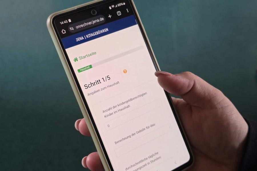 Eine Hand hält ein Smartphone auf dem der Kitagebührenrechner der Stadt Jena geöffnet ist.