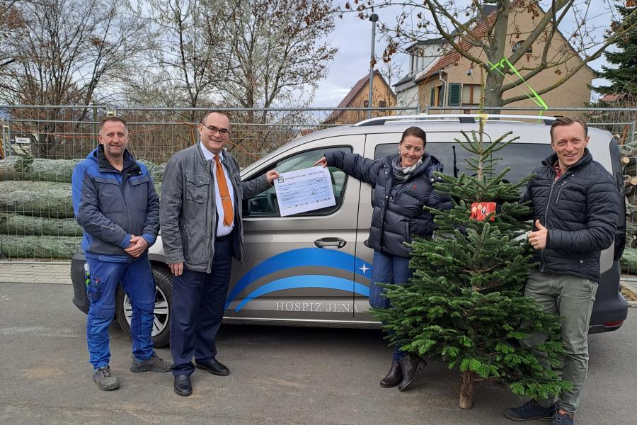 drei Männer und eine Frau stehen mit einem Spendenscheck und einem Weihnachtsbaum vor einem Auto.