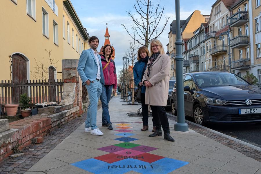 Ein Mann und drei Frauen stehen an einem bunten Hüpfekästchen.