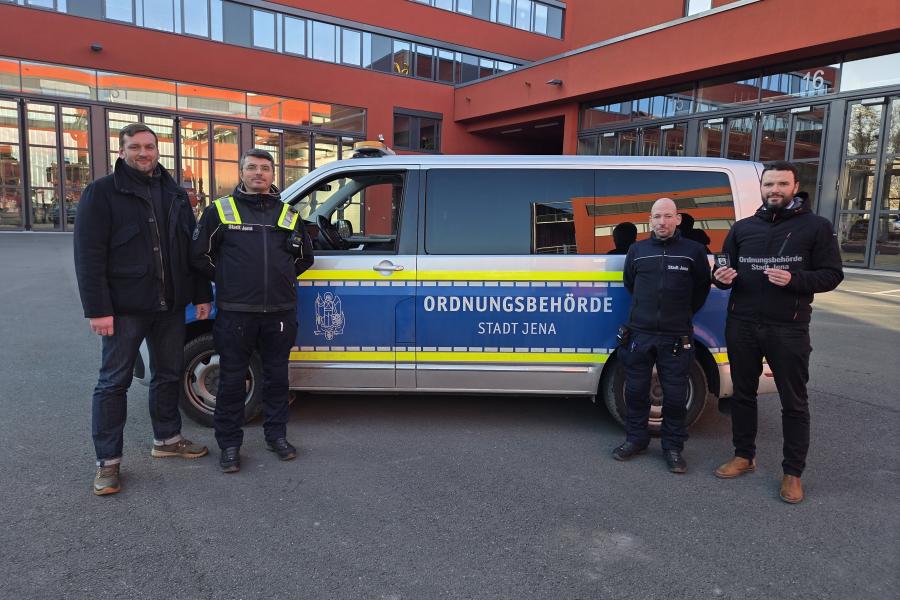 Vier Männer stehen vor einem Auto der Ordnungsbehörde und sehen in die Kamera.