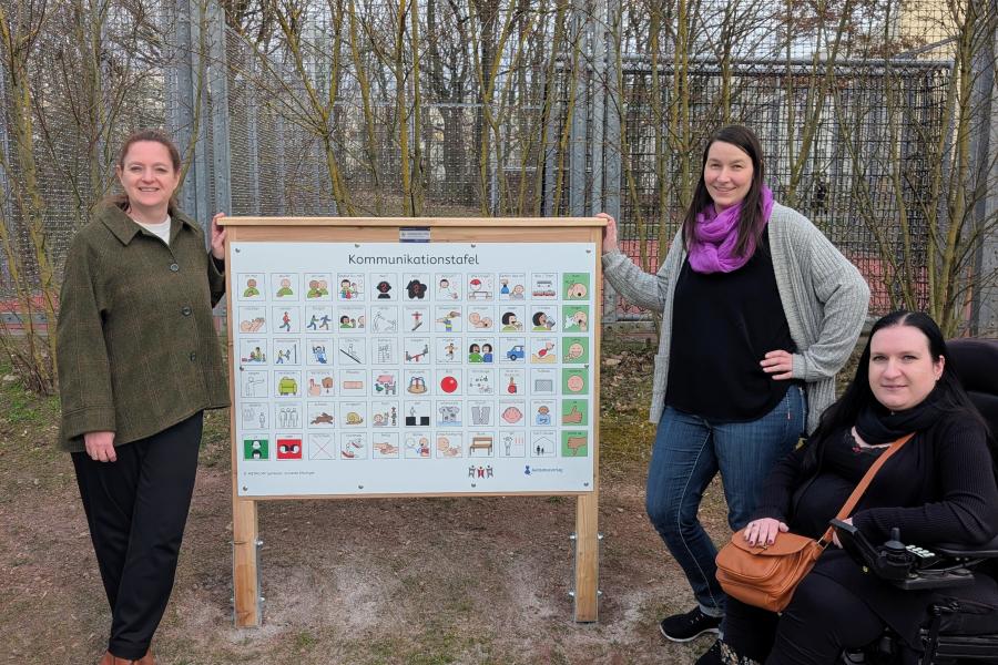 Kathleen Lützkendorf (Dezernentin für Soziales, Gesundheit, Zuwanderung und Klima),  Daniela Egert (Einreicherin des Vorschlags) und Ines Muskalla (Beauftragte für Menschen mit Behinderung der Stadt Jena) bei der Spielplatztafel im Marienwäldchen.
