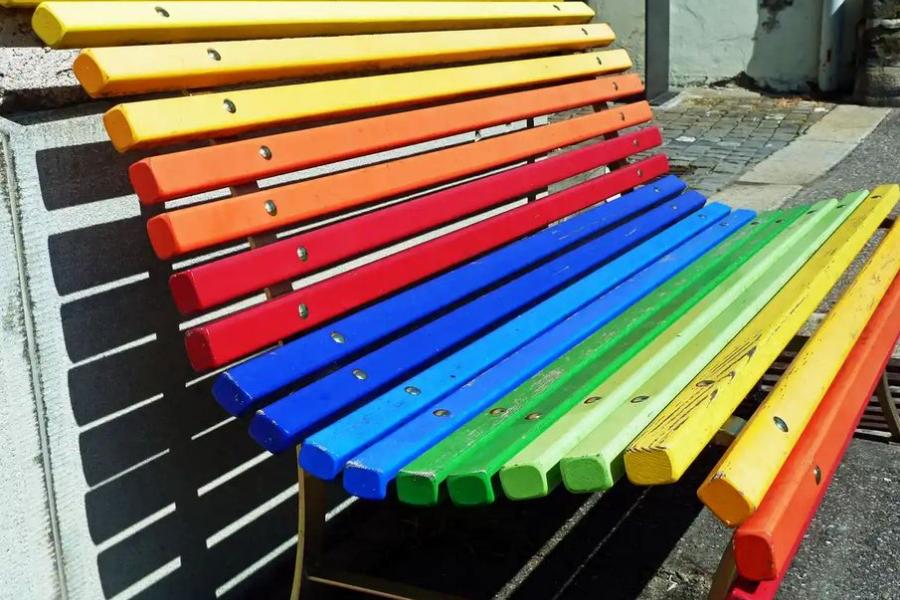 Eine Parkbank, die regenbogenfarben gestrichen ist.