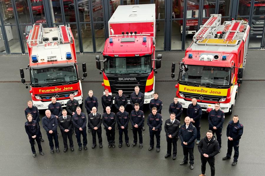 Feuerwehrleute stehen vor drei Autos und schauen in die Kamera.