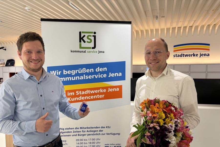 Zwei Männer stehen nebeneinander. Der eine hat einen Blumenstrauß in der Hand.