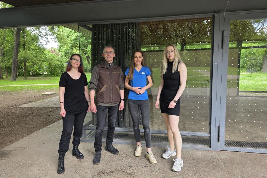 Ein Mann und drei Frauen stehen vor einer Glasfront, die mit Punktfolie gegen Vogelschlag beklebt ist.