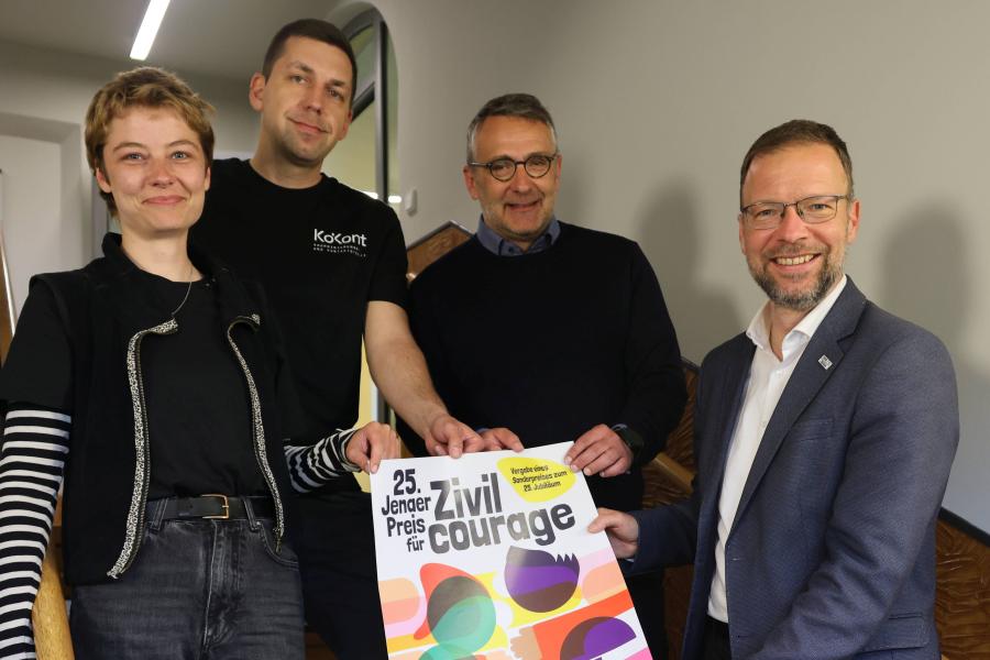 Vier Menschen halten im Treppenhaus ein Plakat.