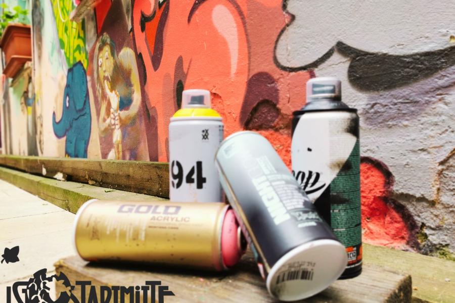 Vier Spraydosen vor einer besprühten Wand