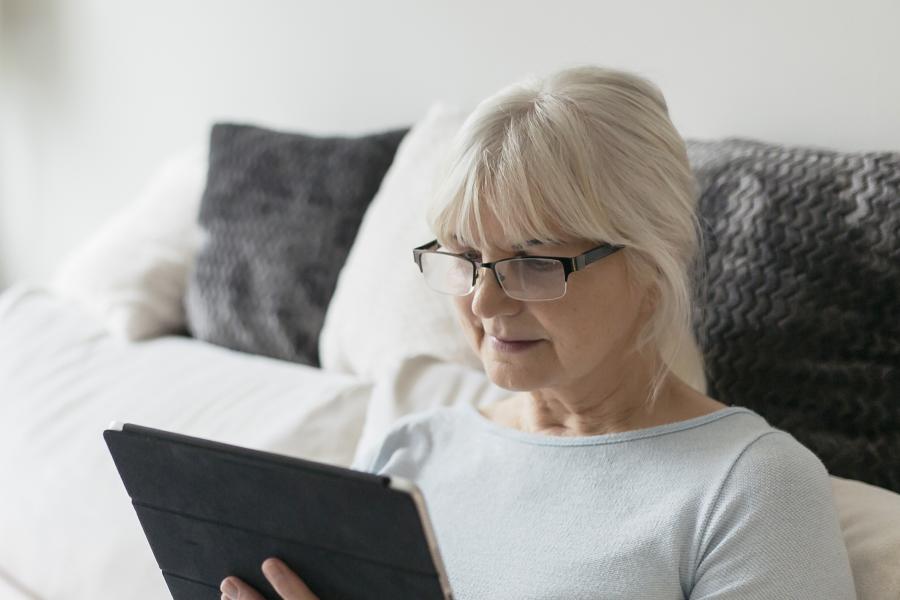 Seniorin sitzt auf einer Couch und surft mit einem Tablet