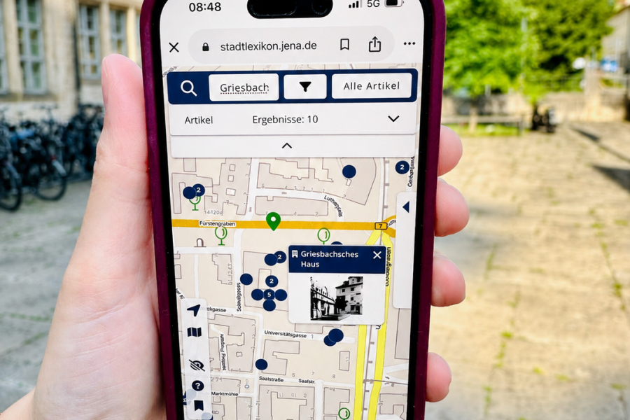Hand hält Smartphone, auf dem eine Stadtkarte zu sehen ist. 