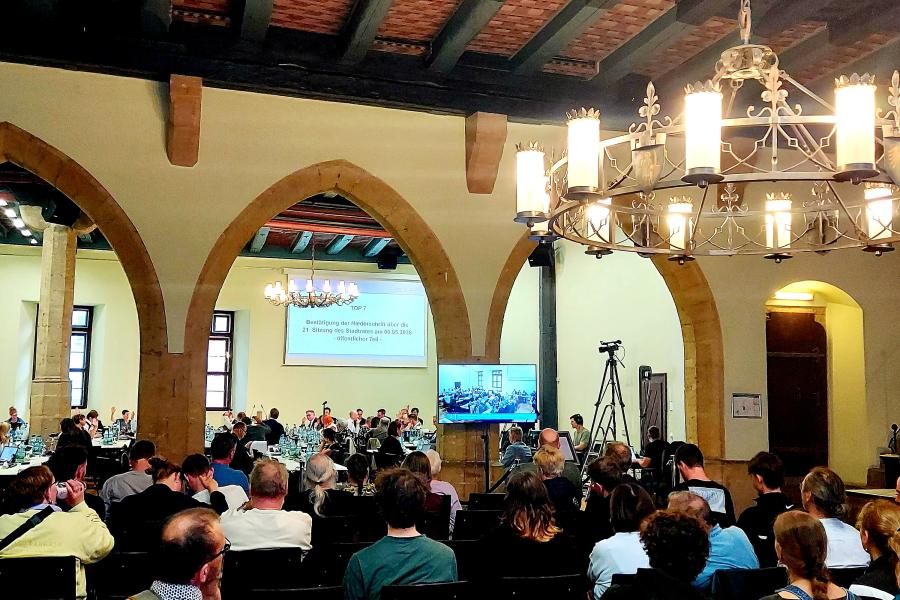 Saal des historischen Rathauses während der Stadtratssitzung mit Menschen auf Stühlen und an Tischen sitzend