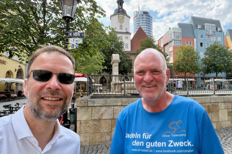 Zwei Männer stehen auf dem Markt in Jena und machen ein Slfie mit Rathaus und Jentower im Hintergrund