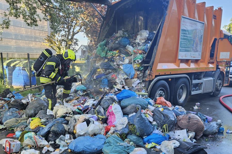 Ein Müllfahrzeug hat den Abfall auf eine Straße gekippt, nachdem die Ladung gebrannt hat. Ein Feuerwehrmann durchsucht den Müll nach Glutnestern.