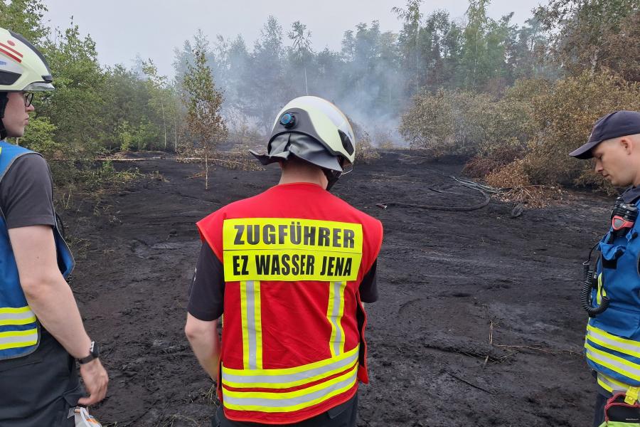 Einsatzkräfte sind von hinten zu sehen vor einer Brandfläche.
