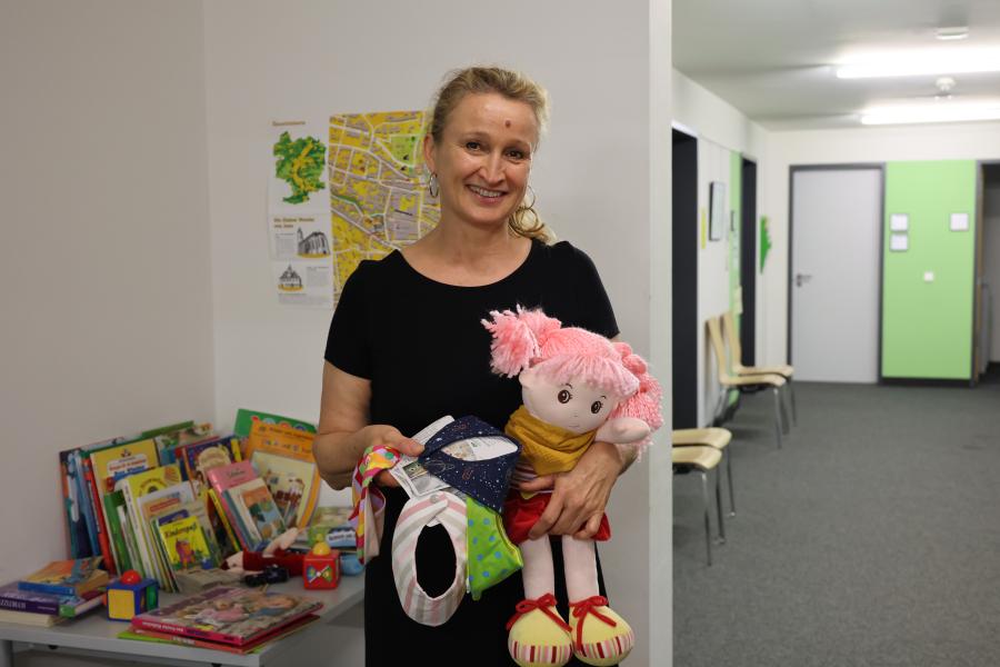 Frau hält Puppe und Halstücher im Arm und lächelt in die Kamera.