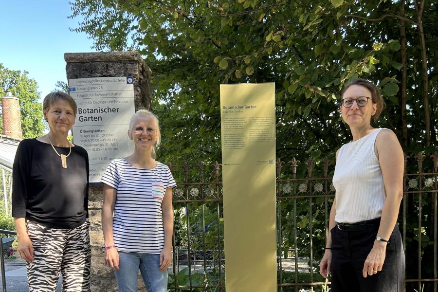 Drei Personen stehen neben einer Stele
