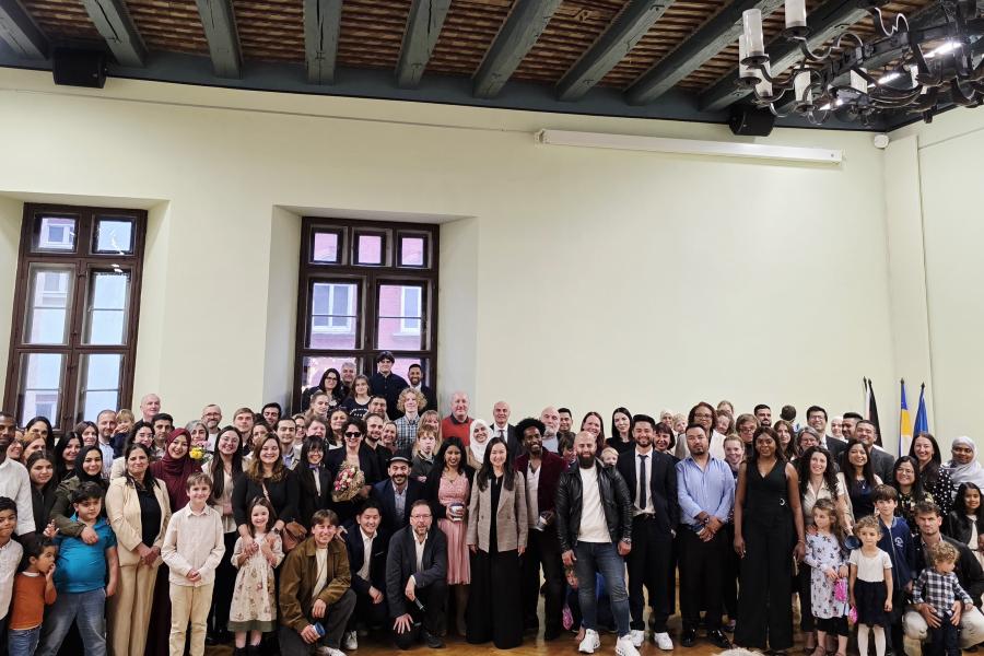 eine Gruppe von Menschen steht vor einer Wand mit zwei Fenstern und feiert ihre Einbürgerung im historischen Rathaus