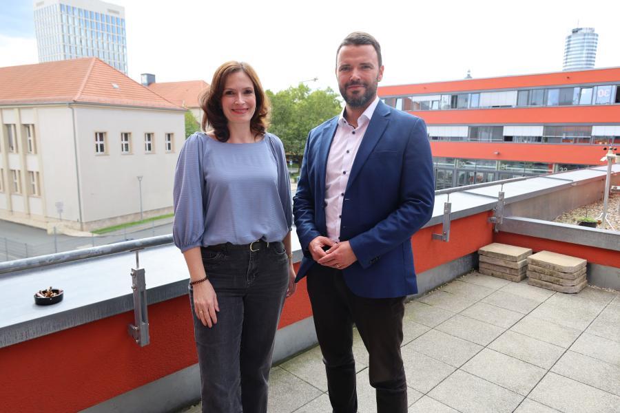 Mann und Frau stehen auf einer Terrasse mit Jena im Hintergrund.