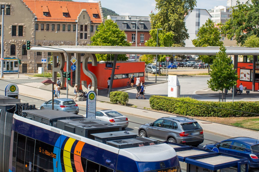  Im Vordergrund eine Straßenbahm im Hinergrund rechts Autos auf der Weigelstraße und der Busbahnhof, im Hintergrund oberhalb der Straßenbahn das Volkshaus Jena
