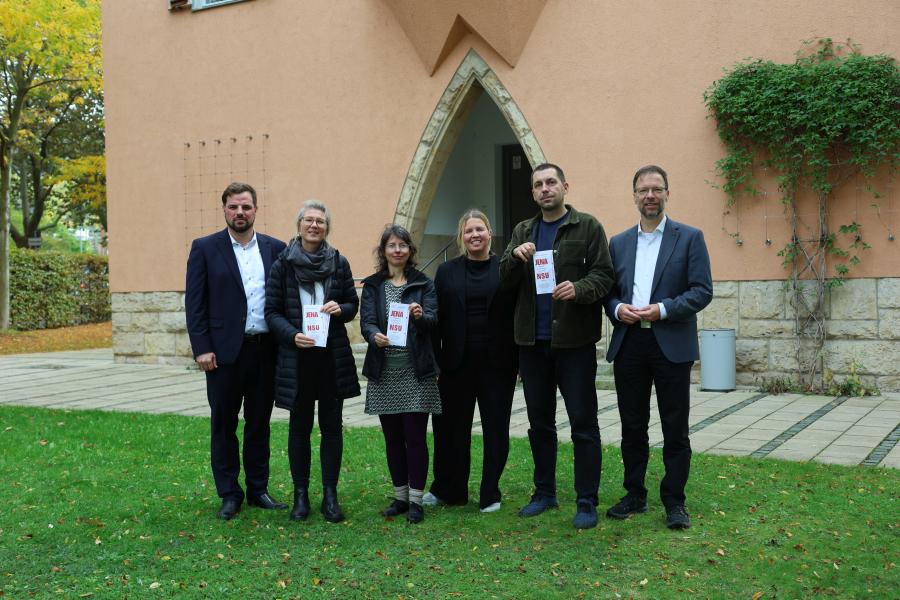 Drei Frauen und drei Männer stehen nebeneinander vor dem Verwaltungsgebäude Am Anger 15, drei halten einen Flyer in der Hand.