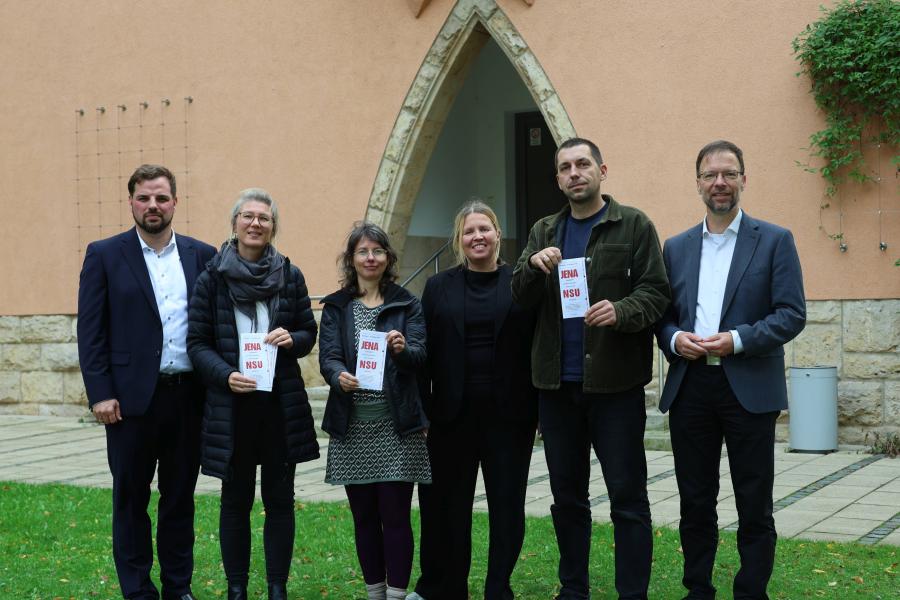 Drei Frauen und drei Männer stehen nebeneinander vor dem Verwaltungsgebäude Am Anger 15, drei halten einen Flyer in der Hand.