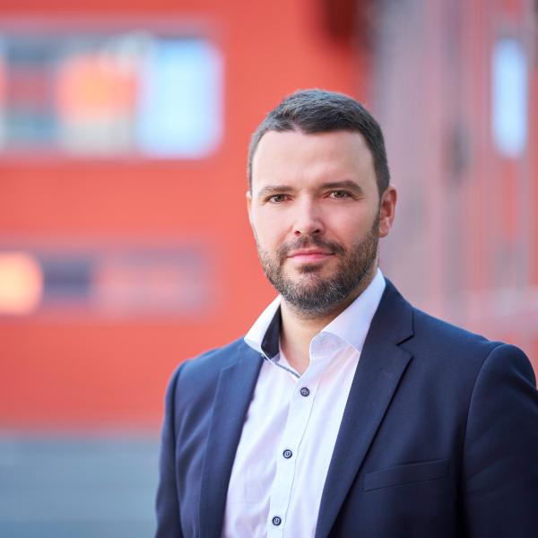 Mann in blauem Anzug steht im Außenbereich und lächelt