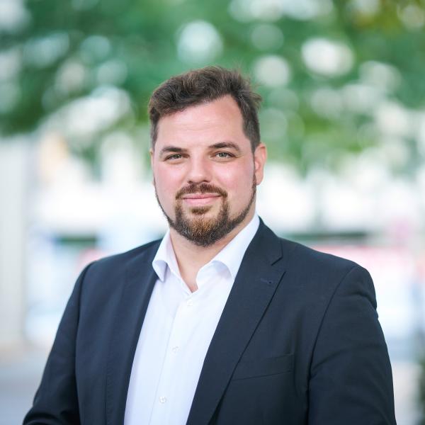 Mann in blauem Anzug steht im Außenbereich und lächelt