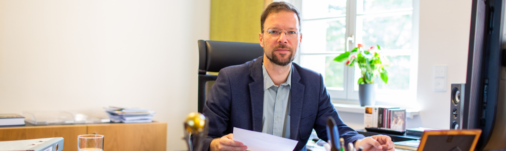 Oberbürgermeister Dr. Thomas Nitzsche sitzt am Schreibtisch in seinem Büro mit einem Dokument in der Hand